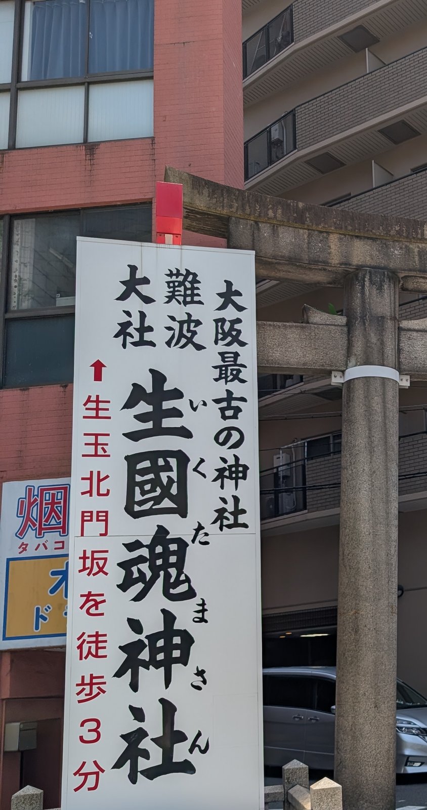 道沿いに立つ生國魂神社の案内看板と、鳥居の柱