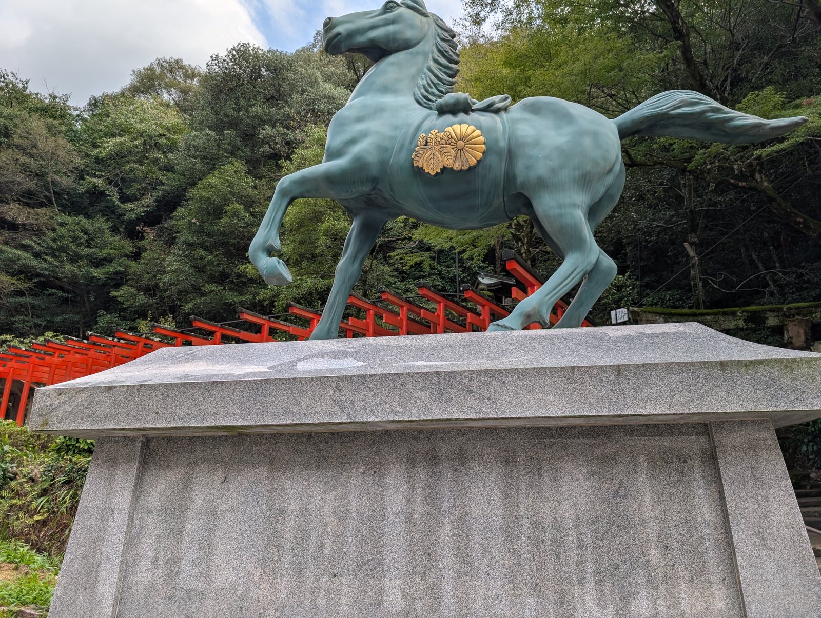 青銅の神馬像。背後の斜面に朱の鳥居が連なる