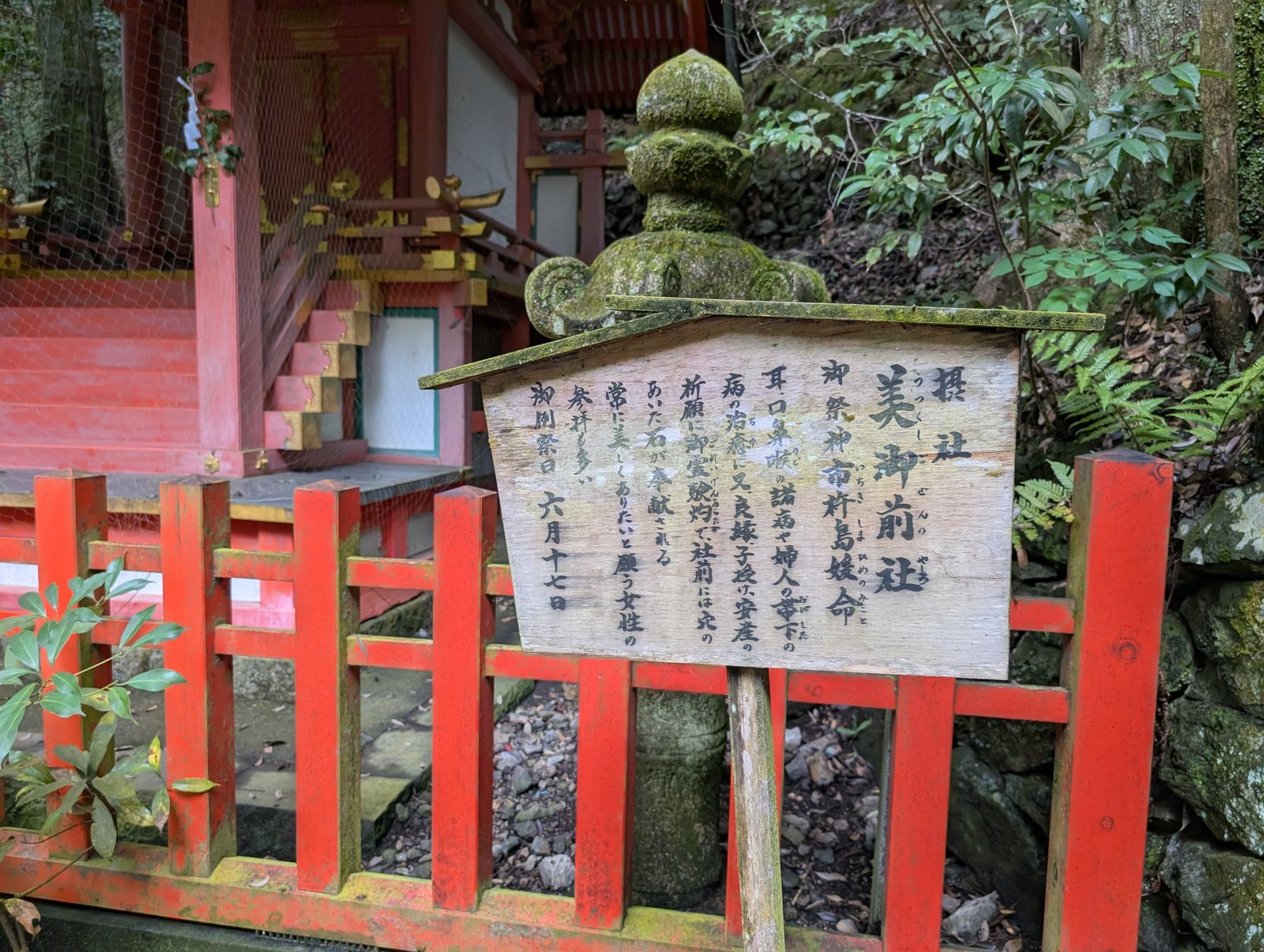美御前社の説明板。朱塗りの玉垣の前に立つ