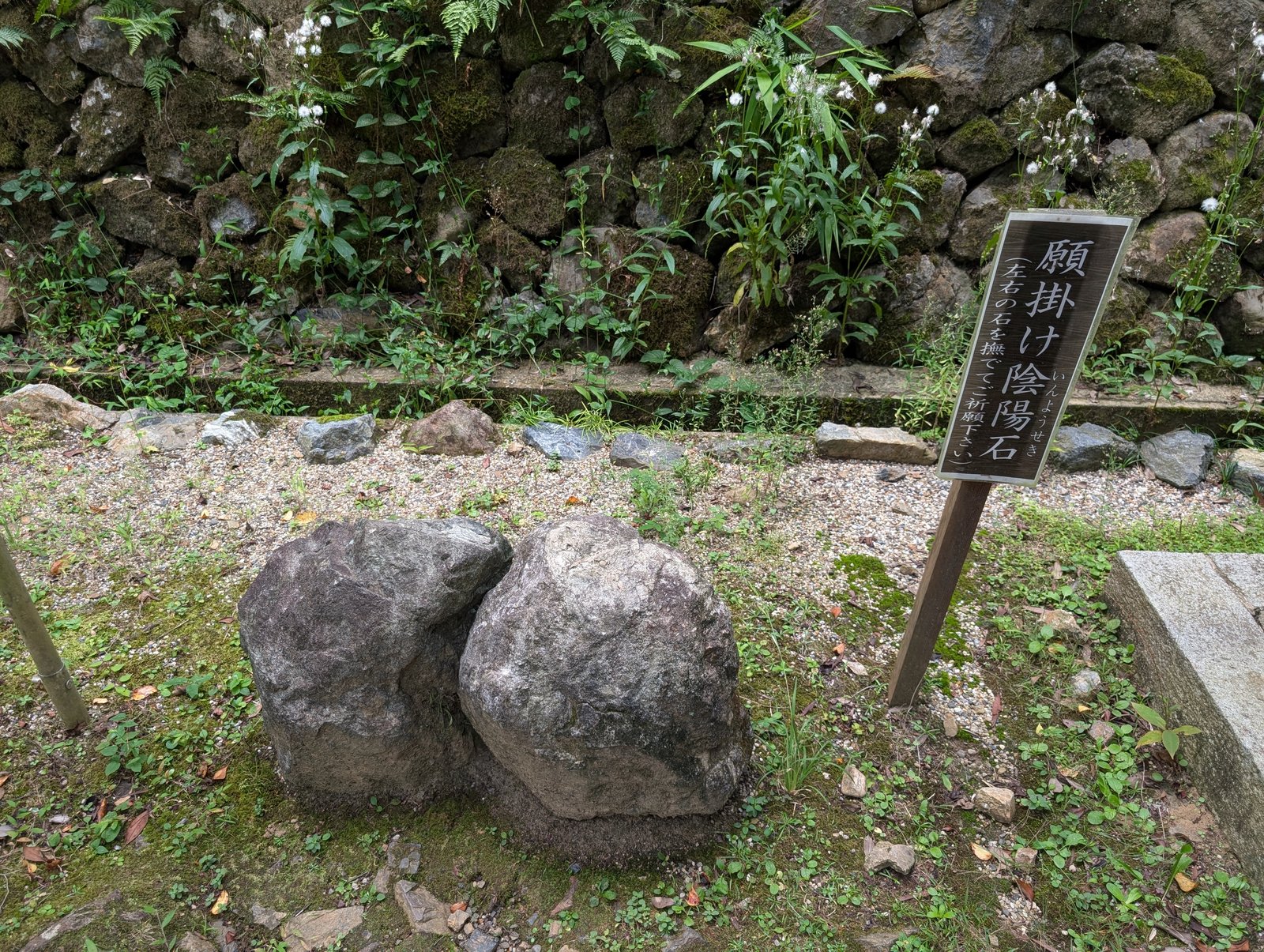 願掛け陰陽石。木の標柱の手前に二つの石が置かれている