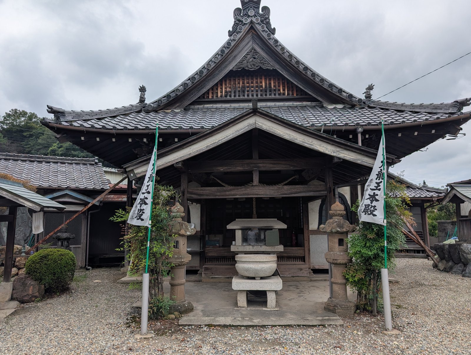 池の対岸に建つ木造瓦屋根の堂。両脇に「八大龍王本殿」の幟