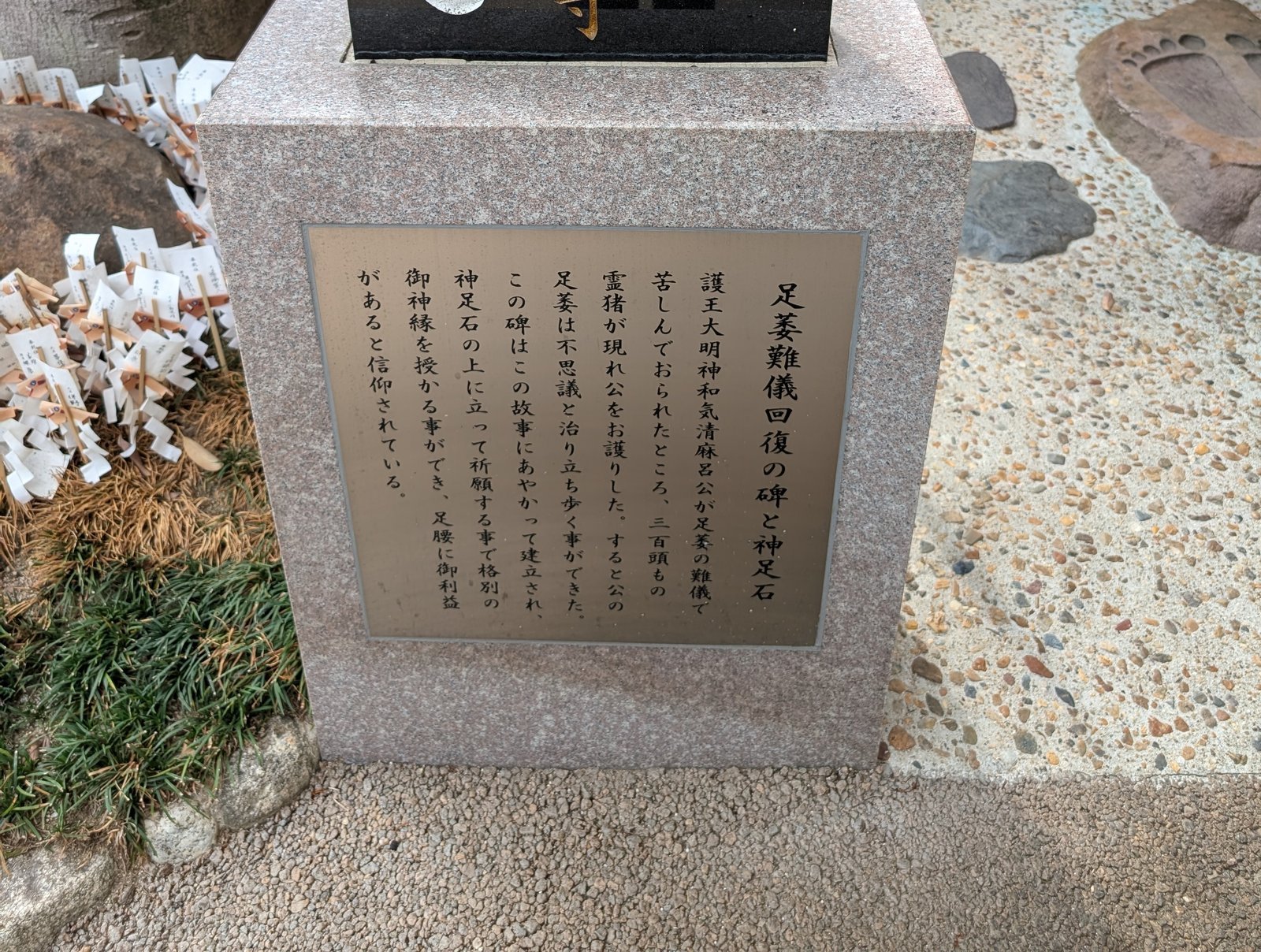 現地の説明板「足萎難儀回復の碑と神足石」。右奥に足形の刻まれた石
